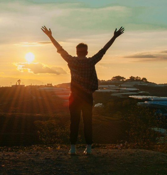 A person celebrating outdoors at sunrise